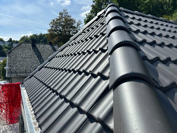 Schwarzes, gewelltes Dach mit Blick auf angrenzende Dächer und blauem Himmel.